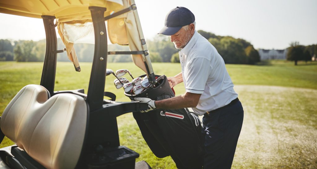 Senior golfer placing his golf club bag onto a cart