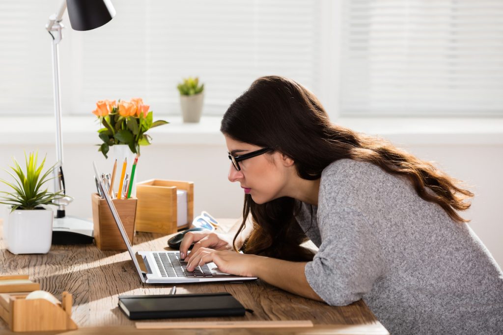 Businesswoman Sitting In Wrong Posture Working On Laptop On Wooden Office Desk.