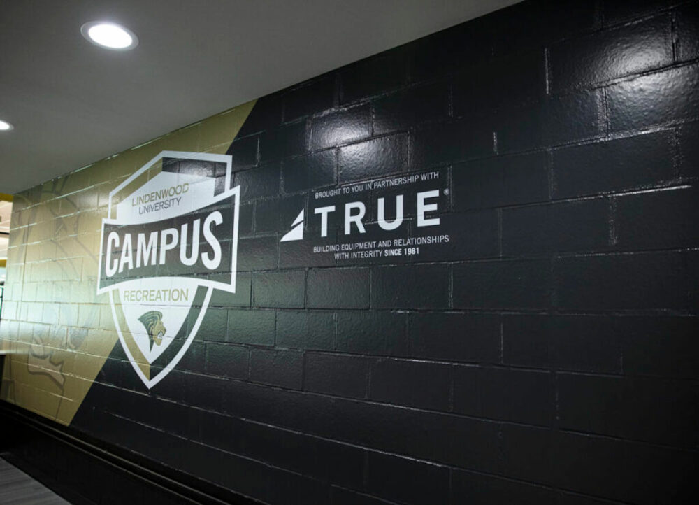 Asociación de la Universidad Lindenwood con TRUE. Logotipos en la pared.