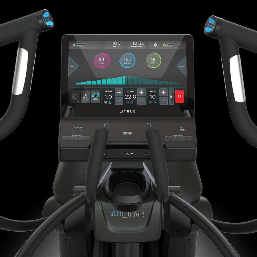 A TRUE Fitness XT-One elliptical machine with a touchscreen displaying controls, progress charts, and other metrics.